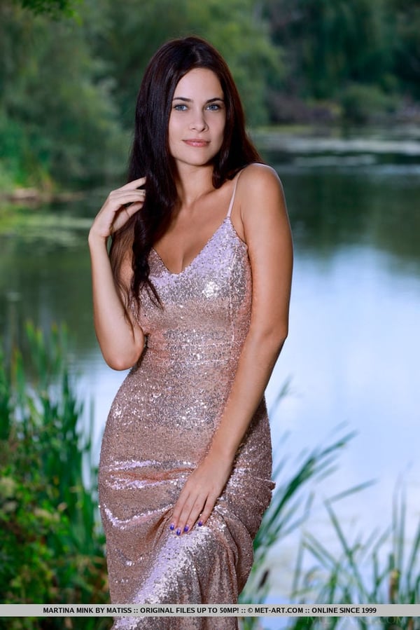 Dark haired teen Martina Mink slips off a long dress to pose nude by a lake
